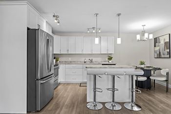 A modern kitchen with a refrigerator, bar stools, and a dining table.